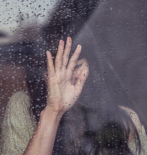 Woman upset looking out of a rainy window