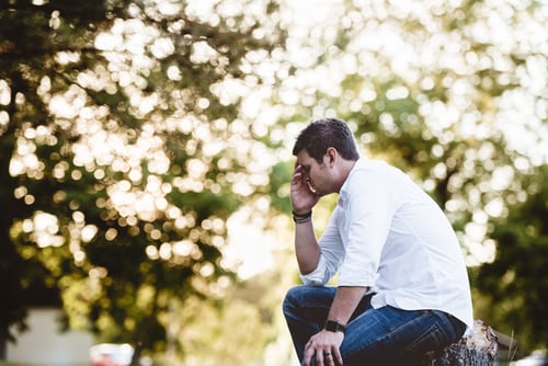 Man sitting on tree stump in forest with head in hand